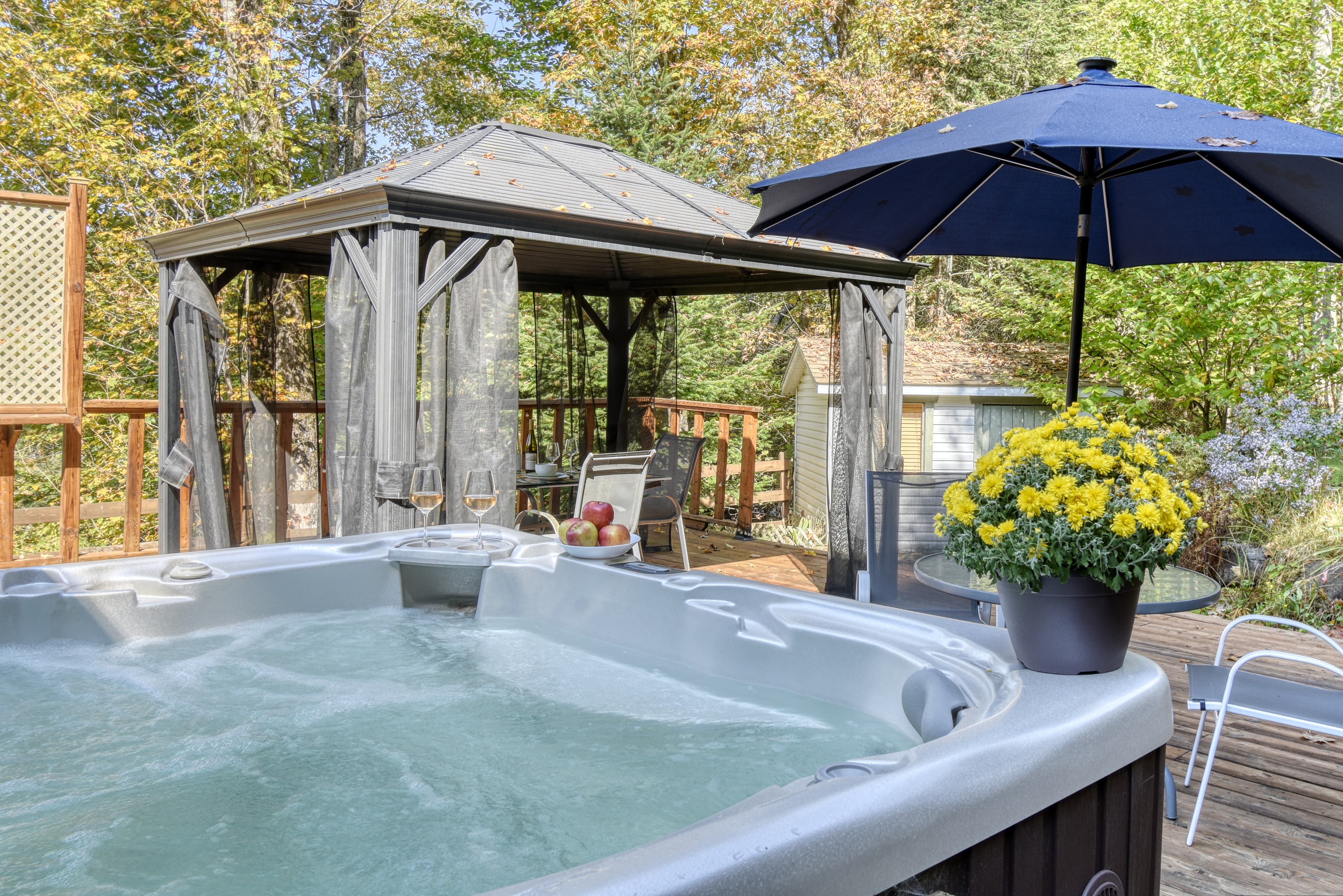 Spa extérieur sur terrasse en bois avec gazebo et vue sur la nature.