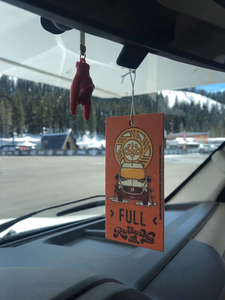 A car dashboard with a sign hanging from the dashboard.