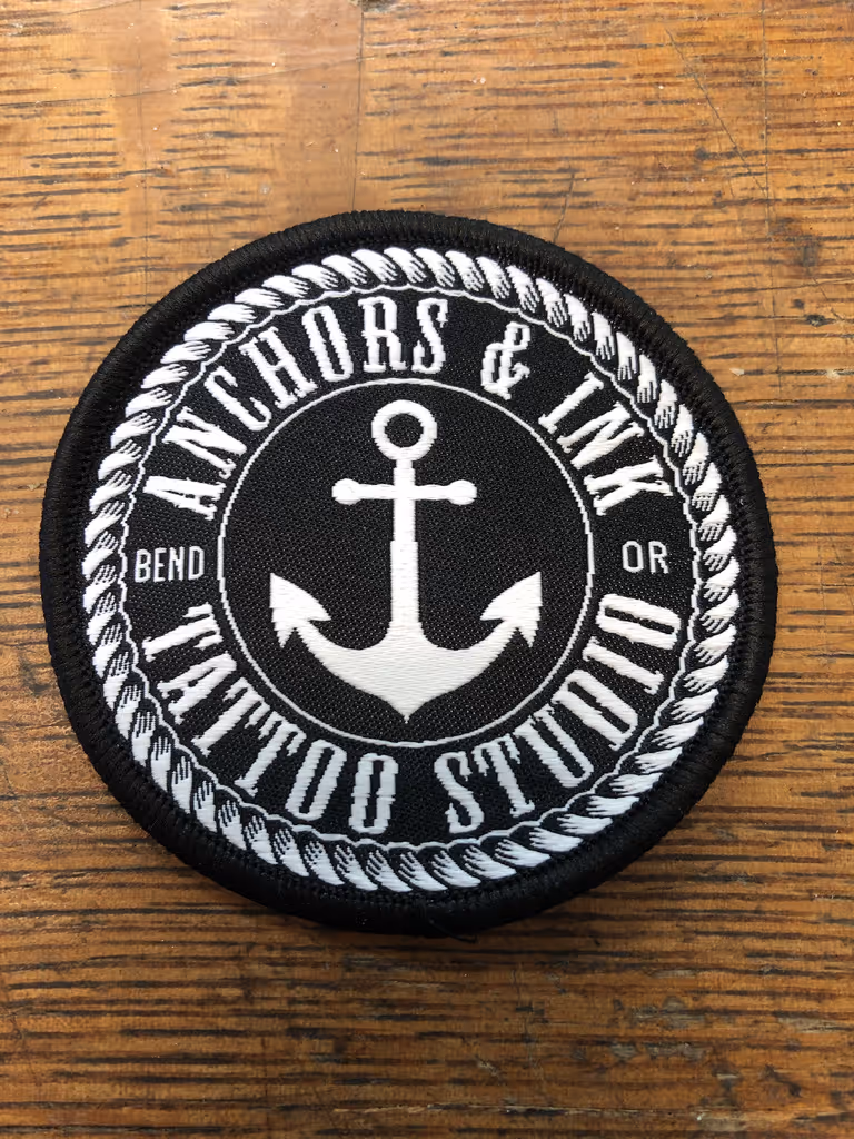A black and white anchor and rope patch on a wooden table.