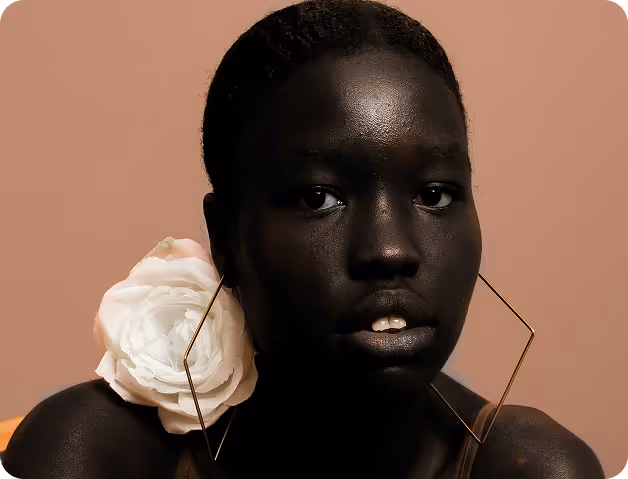 Headshot of a black young woman with large diamond shaped earings and a flower on her shoulder.