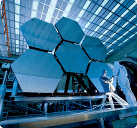 The image suggests precision engineering and high-tech work related to the creation or servicing of a very large and sophisticated telescope or similar optical instrument.