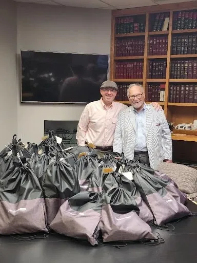 Two men standing behind a table of drawstring bags in a law office