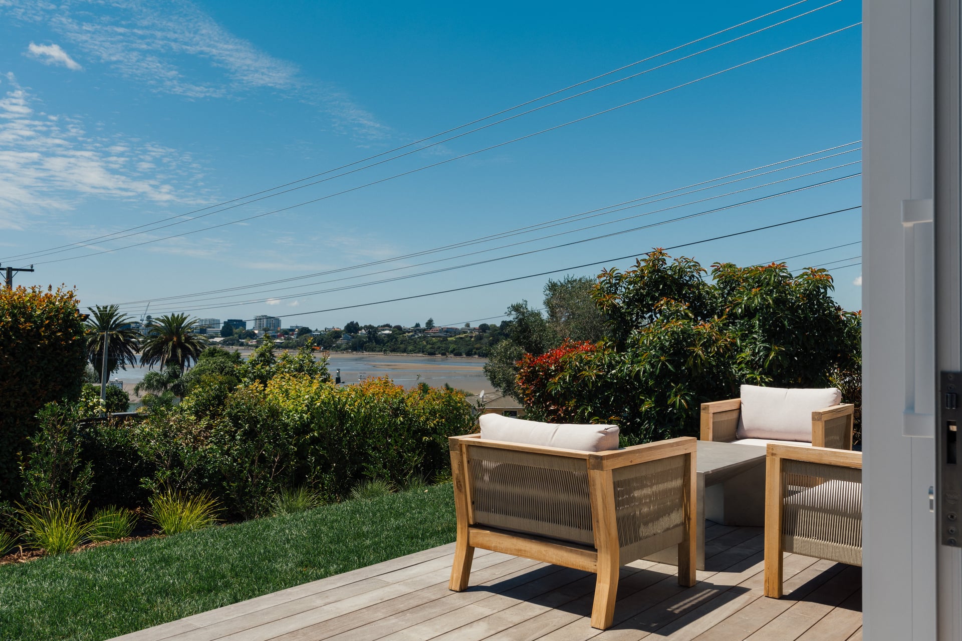 Timber deck with outdoor lounge chairs overlooking harbour views and landscaped gardens at Judea minor dwelling by Gardo Group Tauranga