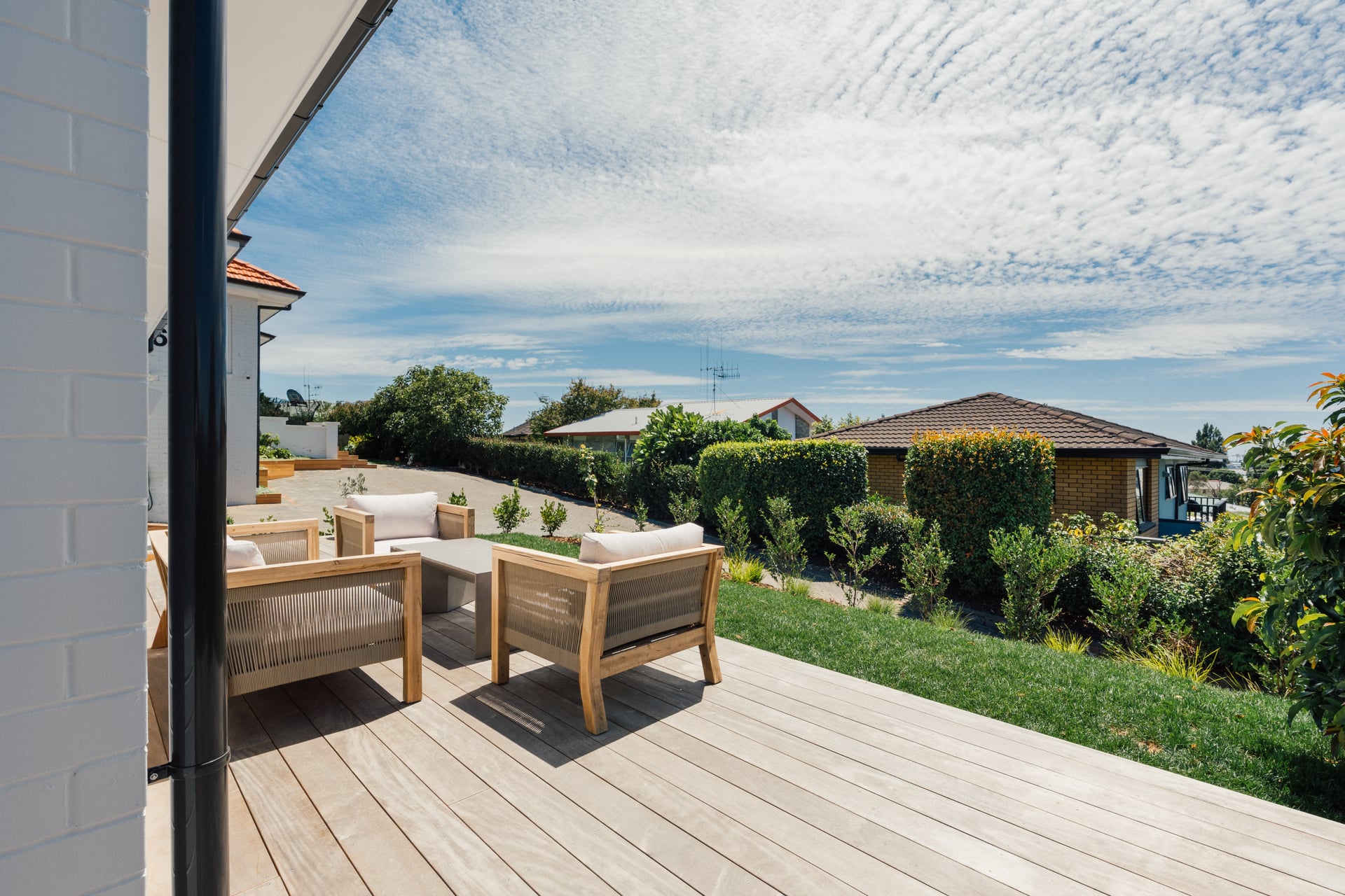 View through sliding glass doors onto timber deck with outdoor lounge furniture and garden views at Judea minor dwelling by Gardo Group