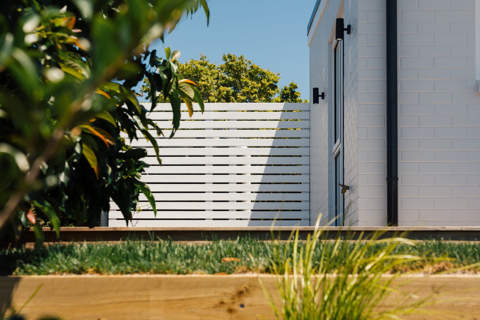 White horizontal slat privacy screen with landscaped garden and timber edging at Judea minor dwelling by Gardo Group