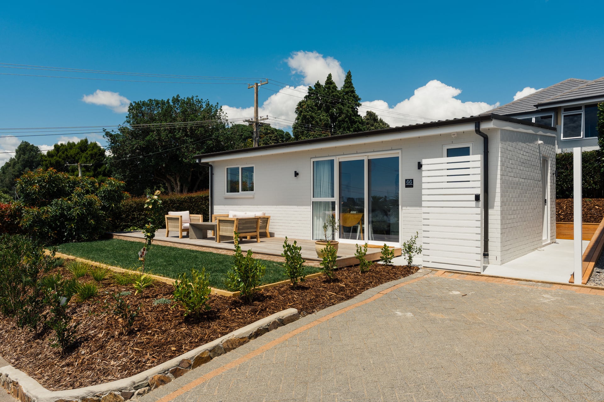 Judea minor dwelling by Gardo Group featuring white cladding, dark roof, landscaped garden and paved driveway in Tauranga