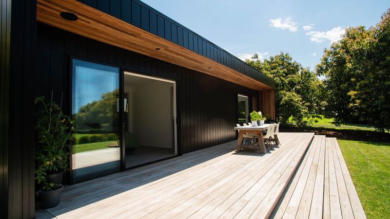 Modern dark-clad home with cedar timber accents wide timber deck and outdoor dining area built by Gardo Group in Tauranga