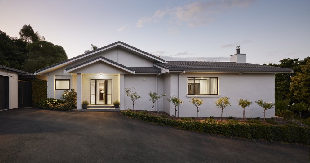 Renovated single storey Te Puna home with a light rendered exterior, tiled hip roof and espaliered trees along a clipped hedge