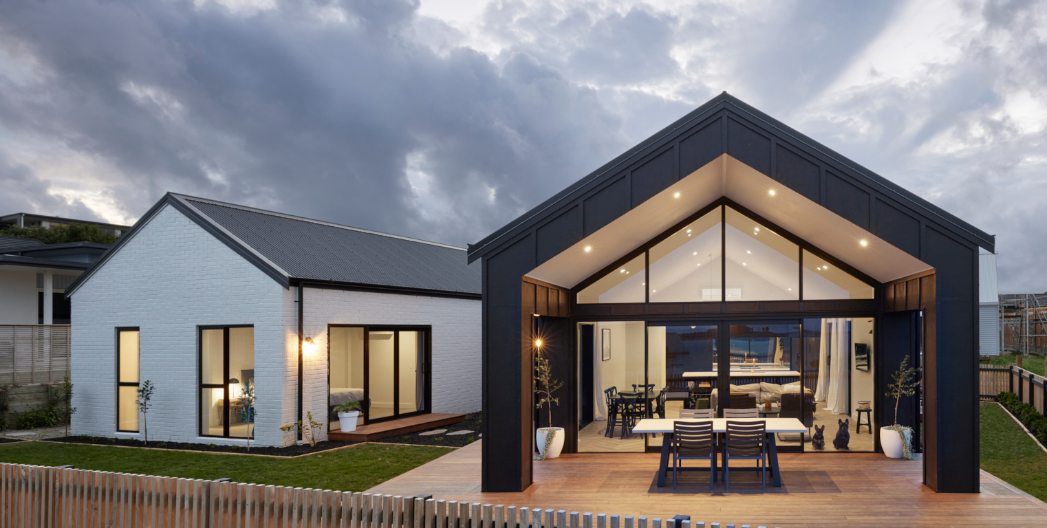 White brick and dark board and batten gables with a glazed gable end and timber deck at dusk, The 15 degree House by Gardo Group