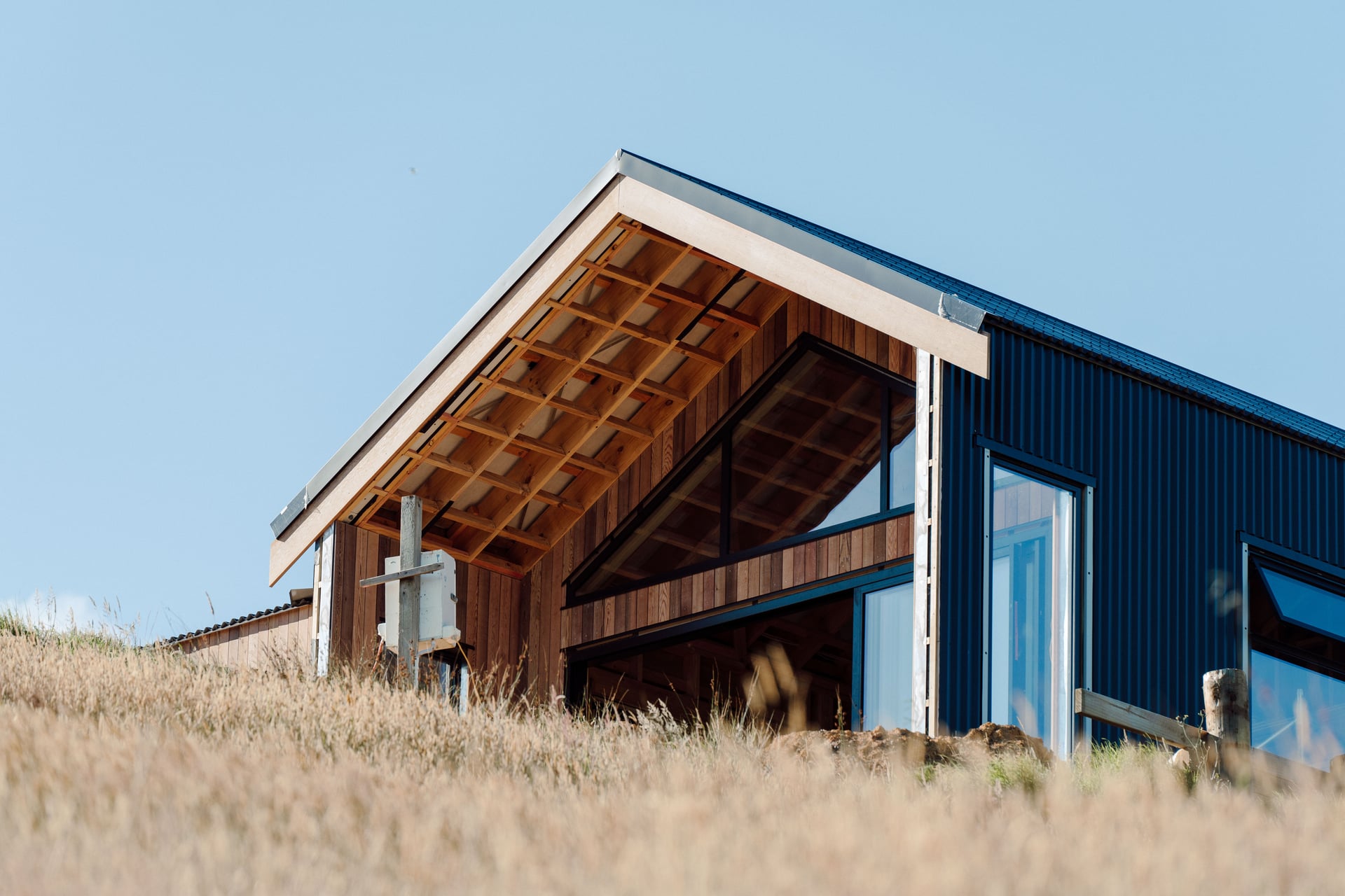 Gable end under construction at Opito Bay showing exposed timber rafters, cedar cladding and dark corrugated steel