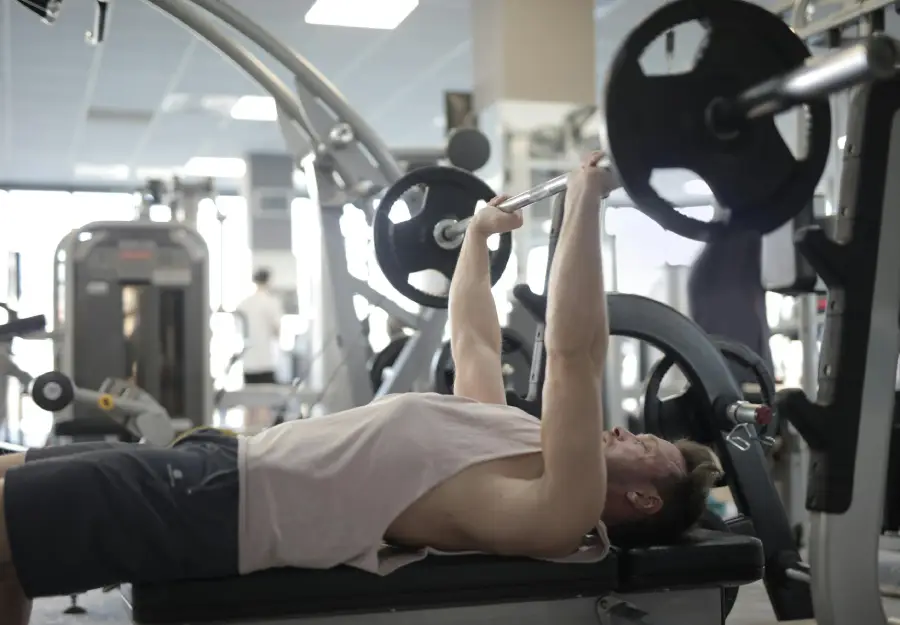 Person performing a bench press exercise with a barbell at a gym, focusing on upper body strength training using free weights.