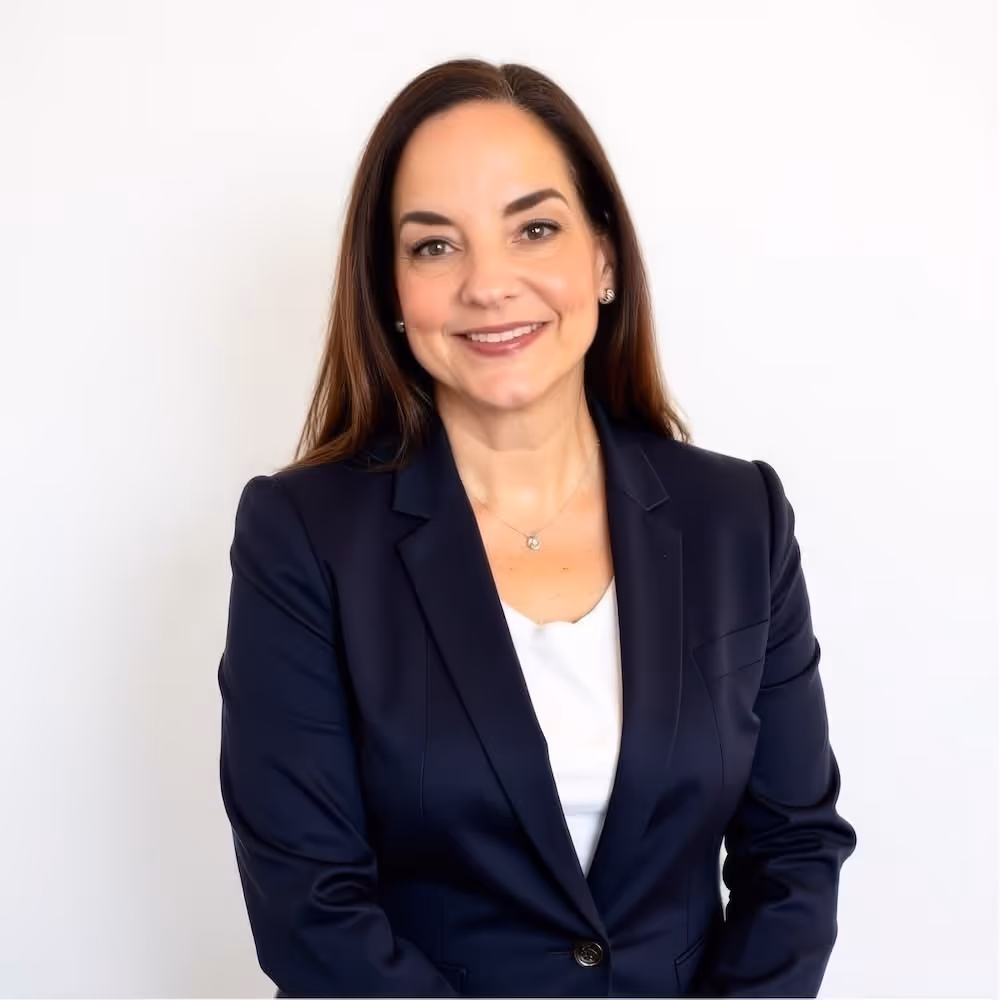 Smiling woman with long brown hair wearing a navy blazer and white top against a white background.
