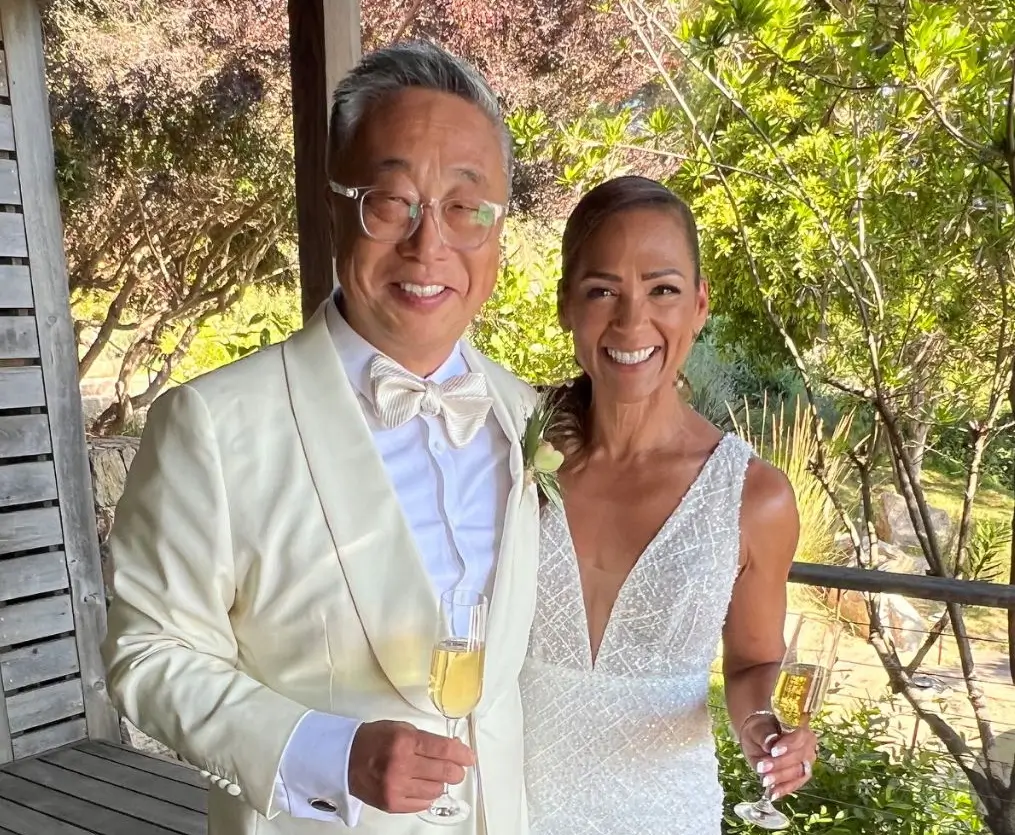 Wedding couple holding a glass of champagne, smiling and posing for a photo shot by guest