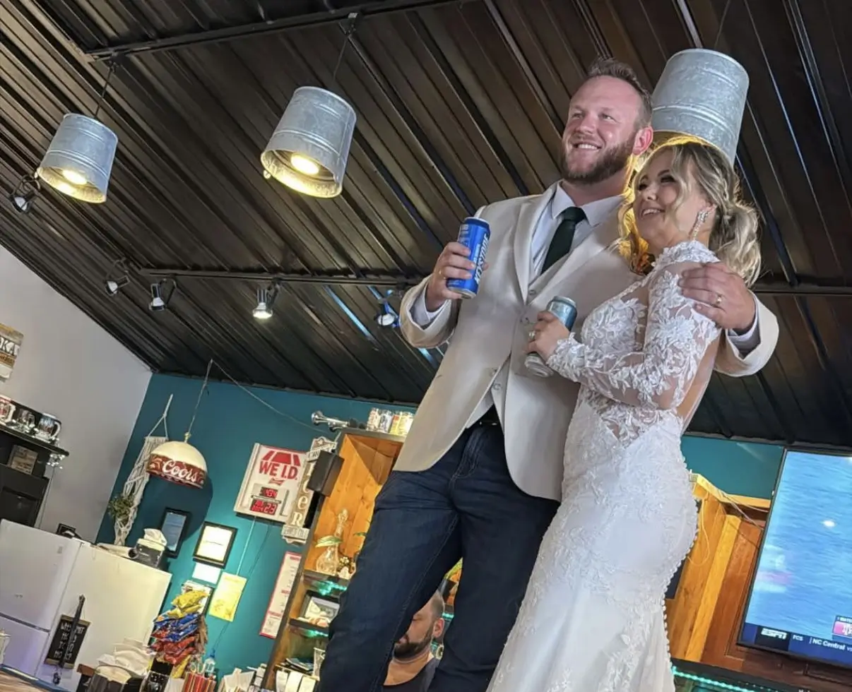 Wedding couple standing on a reception bar table holding drinks - photo taken by a guest