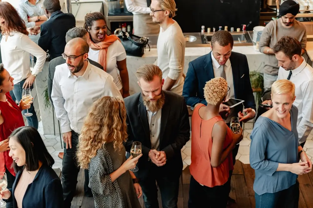 Guests mingling and chatting at a company social event, holding drinks in a bright indoor space