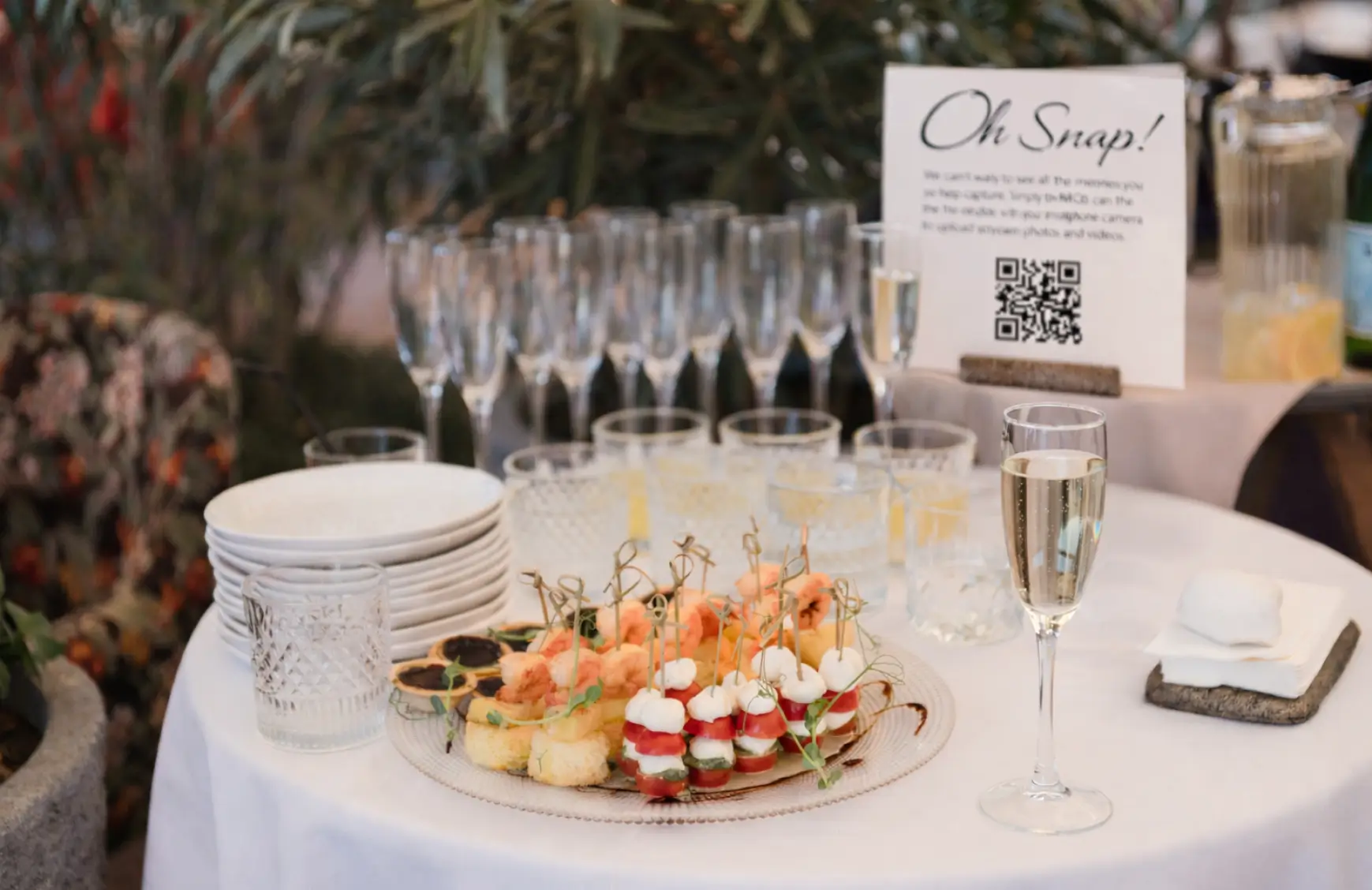 A QR code photo-sharing sign placed naturally at a wedding cocktail hour — making it easy for guests to capture and upload memories.