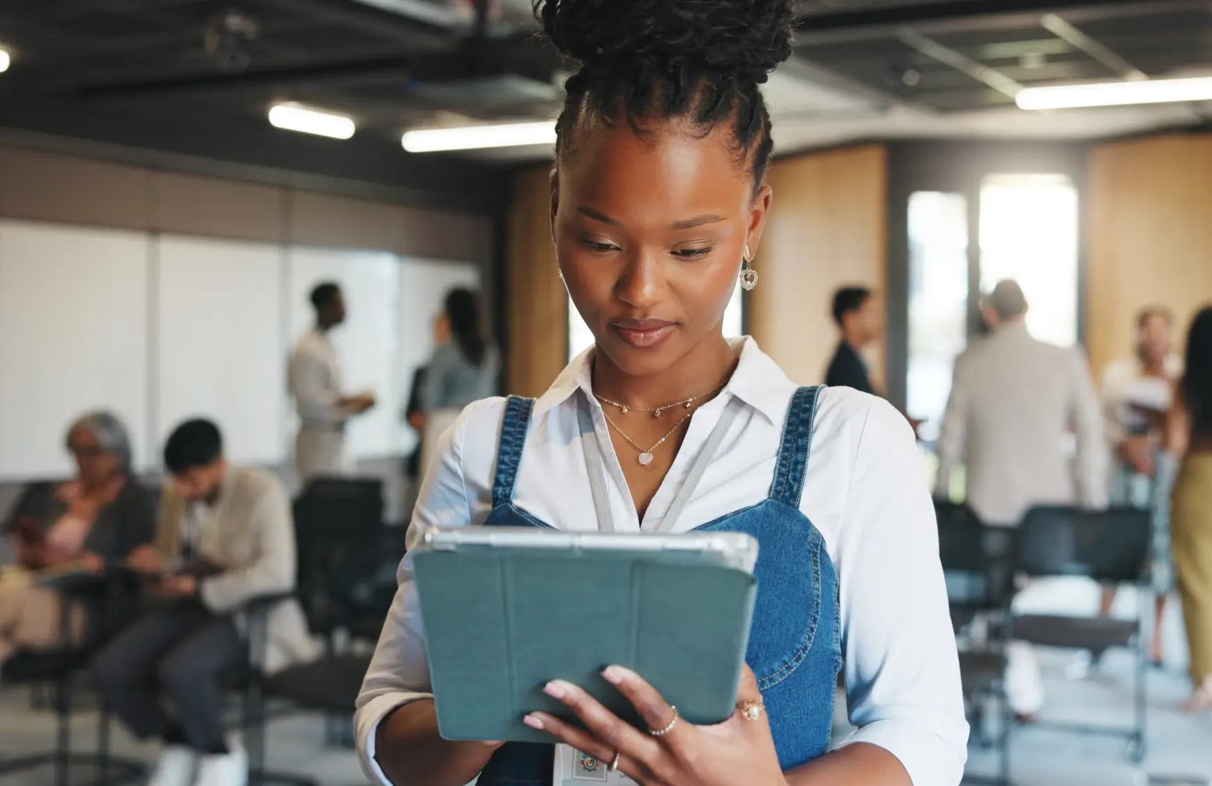 An event organizer reviewing a tablet at a corporate event, with attendees networking in the background.