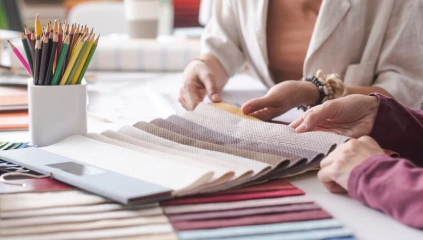 Two women are choosing material for their clothing brand from some fabric swatches