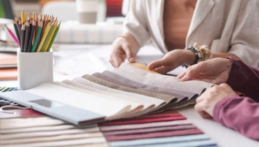 Two women are choosing material for their clothing brand from some fabric swatches