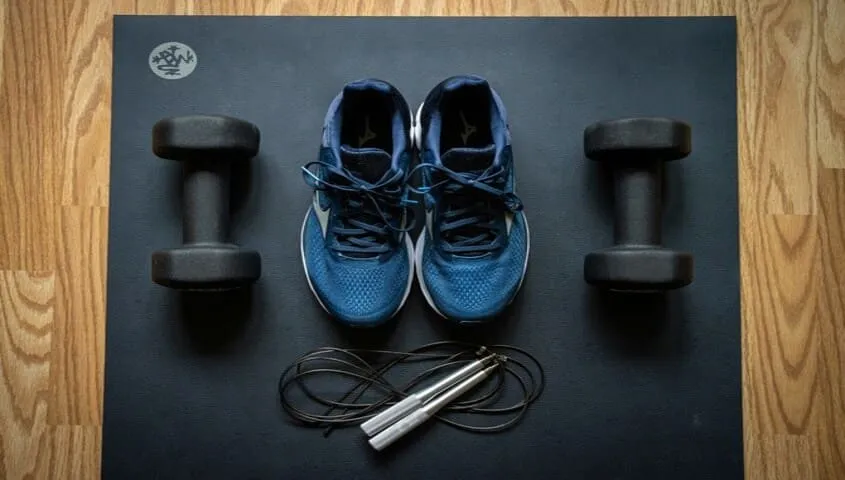Weightlifting dumbbells and sports shoes are placed on the yoga mat.