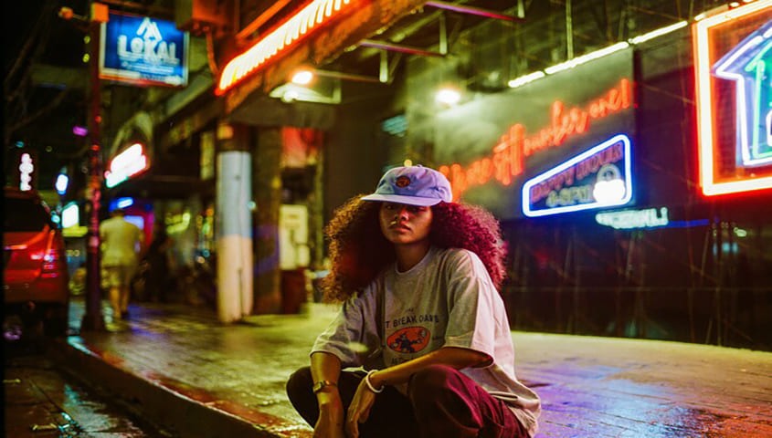A woman is sitting on the street, wearing streetwear style Gen Z fashion clothes.