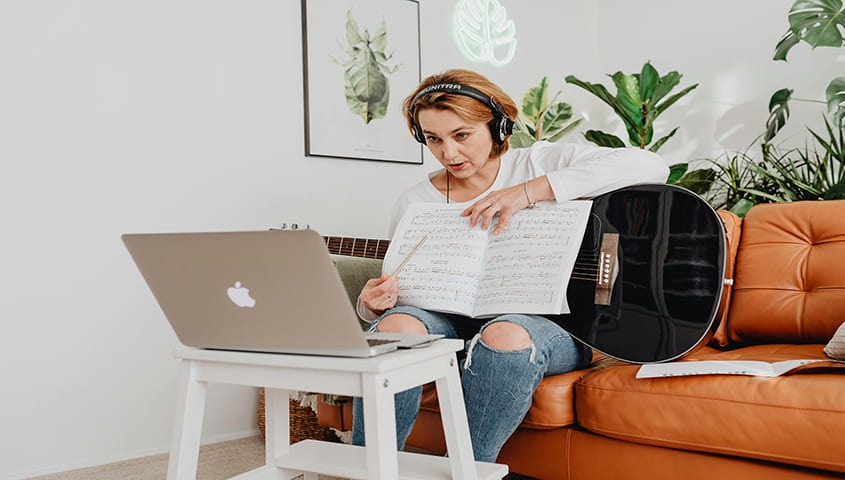 A woman is giving guitar online course on a computer.