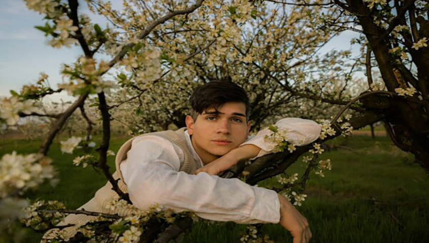 Gen Z cottagecore fashion style, man relaxing against a tree branch