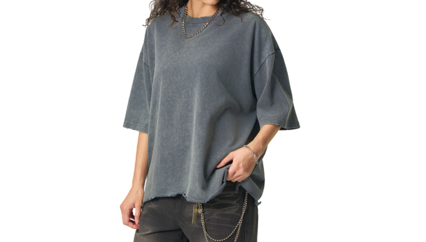 A model wearing an oversized vintage wash boxy t-shirt in slate grey with a raw hem, styled with dark pants and a chain necklace.