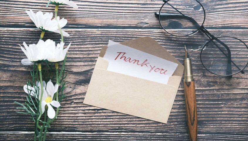 Handwritten thank you for supporting my small business card in a kraft envelope with white daisies and a fountain pen.