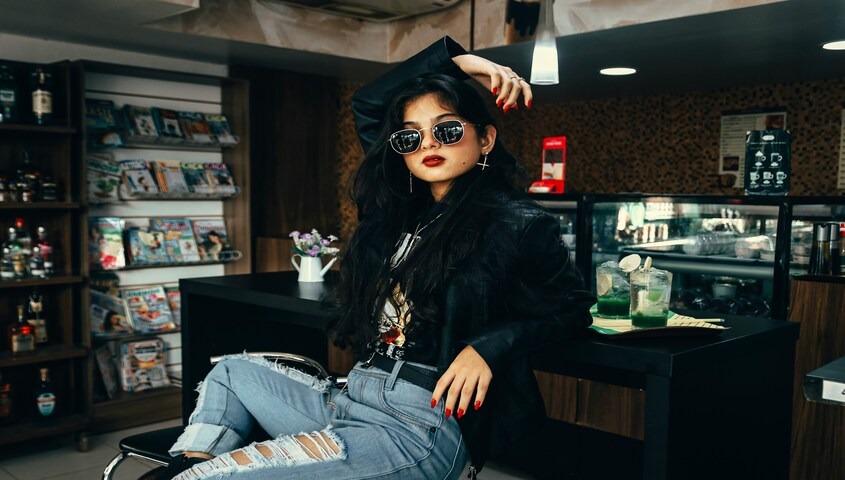 Woman in leather jacket and distressed denim showing classic 90s fashion trends in a moody cafe setting