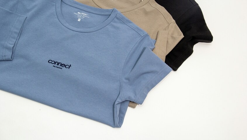 Three premium blank t-shirts in blue, tan, and black folded flat, showing a custom branded logo — ideal for print-on-demand and custom apparel businesses built on quality blanks