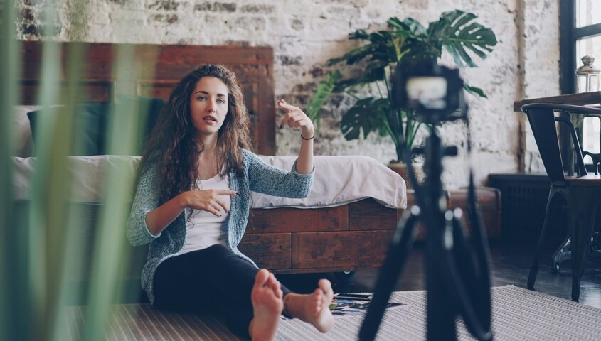 Content creator speaking to a camera on a tripod in a natural home studio, building an audience around affiliate marketing and passive income