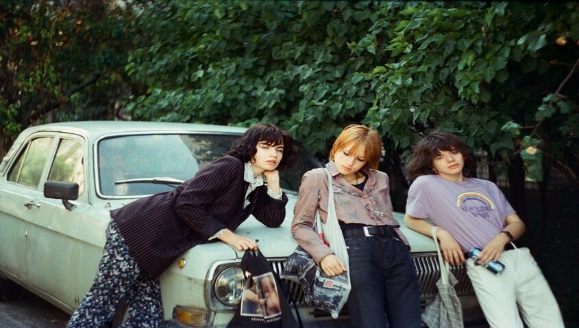 Three people in 70s outfits leaning on a vintage car, a modern take on 70s fashion ideas
