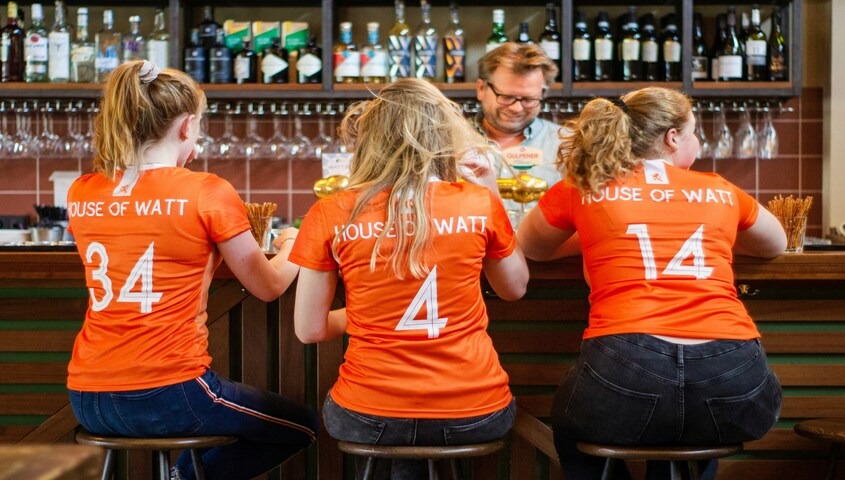 Three family members wearing custom-numbered orange jerseys at a bar, showing how sports-style family reunion t shirts turn a reunion into a roster.