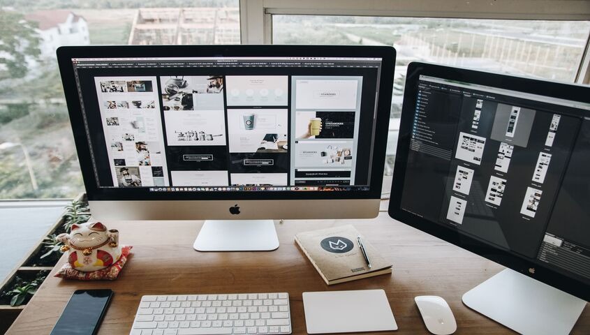Desk workspace with a dual-monitor site build in progress, showing the Wix vs Squarespace decision every apparel founder makes early.
