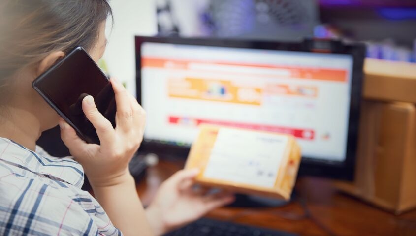 Shopper on the phone reviewing a package next to an online storefront, showing where the real work of how to increase ecommerce sales actually begins.