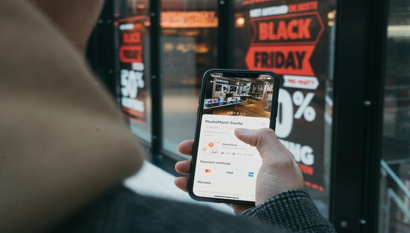 Customer checking business reviews on a phone in front of Black Friday signage, showing how social proof anchors the best ecommerce sales strategies.