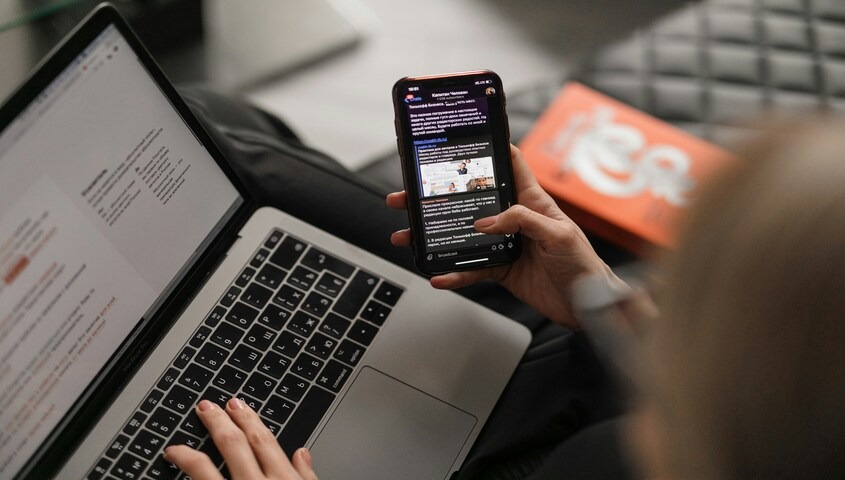 Creator checking TikTok on a phone beside a laptop, mapping the best time to post on TikTok by weekday