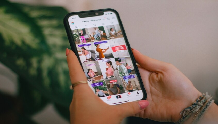 Hands holding a phone showing a grid of TikTok videos, planning the best times to post on TikTok