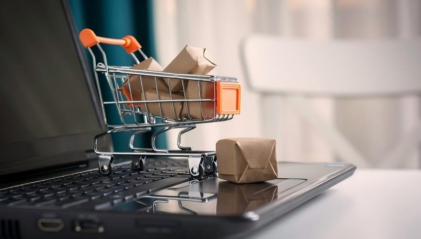 Mini shopping cart with packages resting on a laptop keyboard.