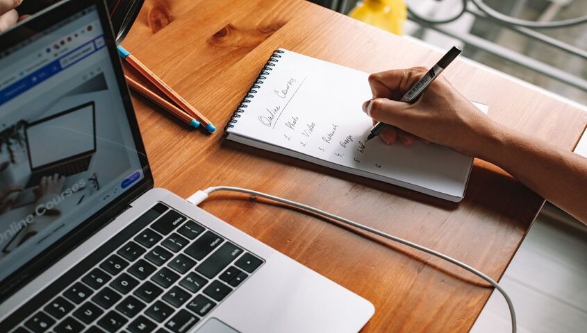 Laptop next to a handwritten online-course plan on a notebook, showing why online courses are among the best small business ideas for long-term earning.