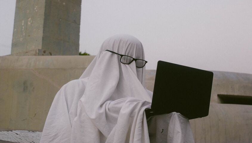 Person in a ghost costume typing on a laptop, a playful take on ghostwriting as a business to start with no money.