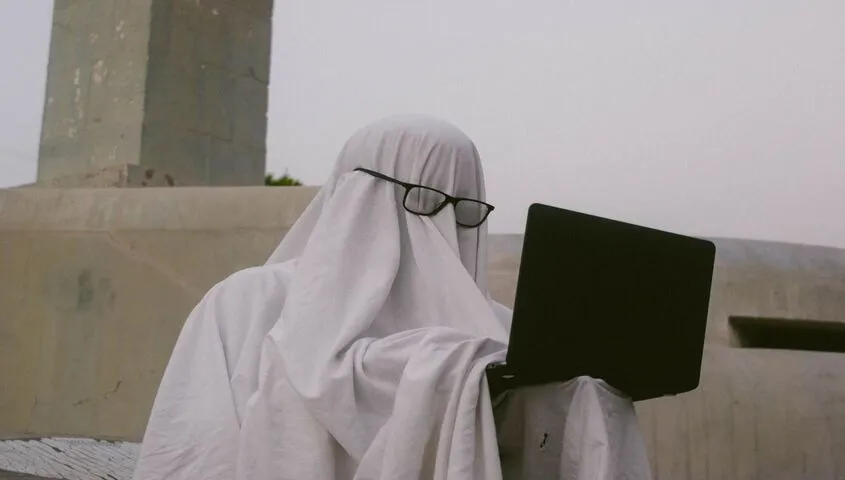 Person in a ghost costume typing on a laptop, a playful take on ghostwriting as a business to start with no money.