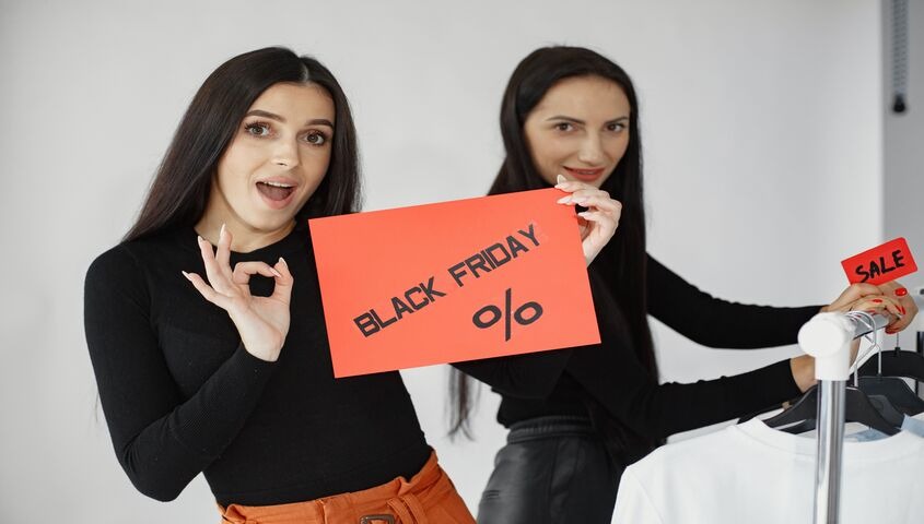 Two shop owners holding a red Black Friday sale sign, kicking off a black friday marketing plan for 2026.