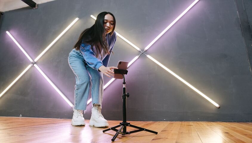 Creator setting up a phone on a tripod under neon lights, starting a TikTok channel with no money down.