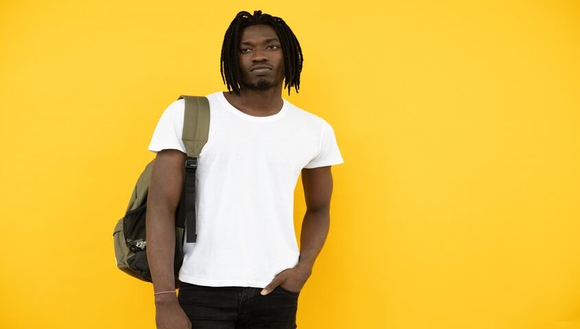 Man in a plain white tee against a yellow wall, the budget lane of the high quality t shirts market.