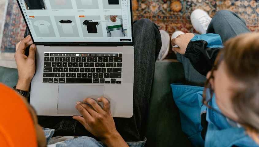 Two people browsing online clothing store on a laptop from above
