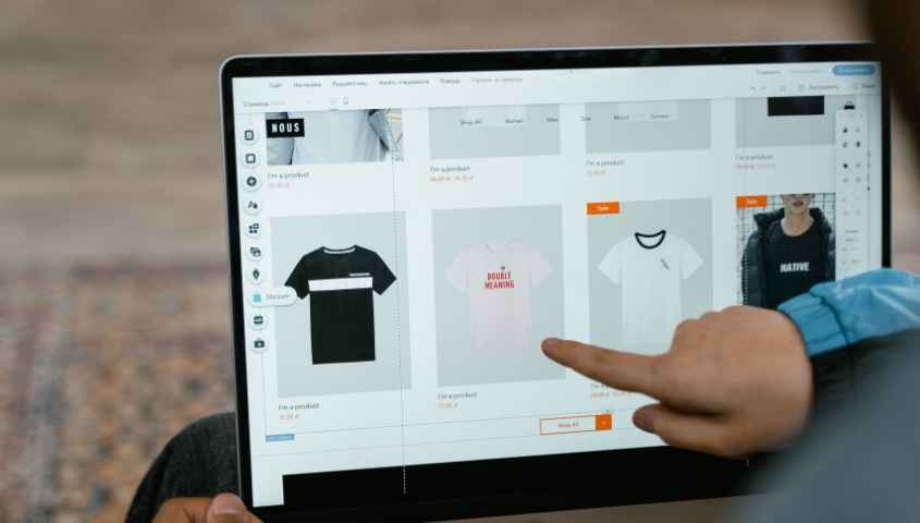 A person points to t-shirt options in an online store on a laptop screen