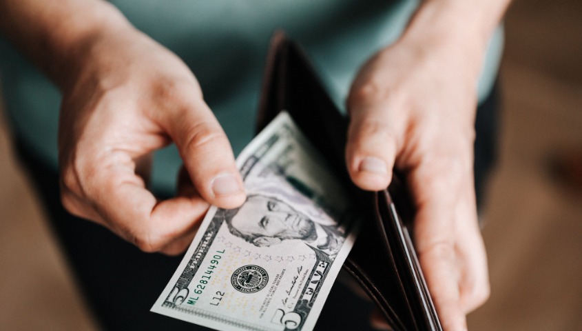 A person taking a five-dollar bill from a wallet