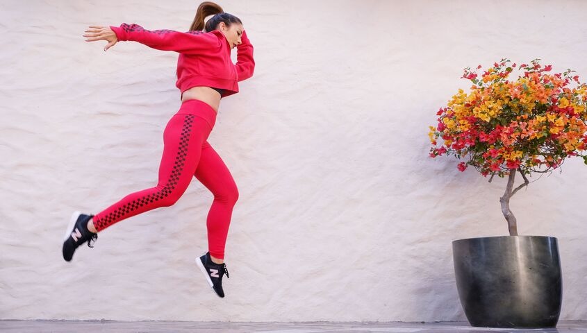 Woman jumping in a red athleisure matching set of cropped hoodie and printed leggings